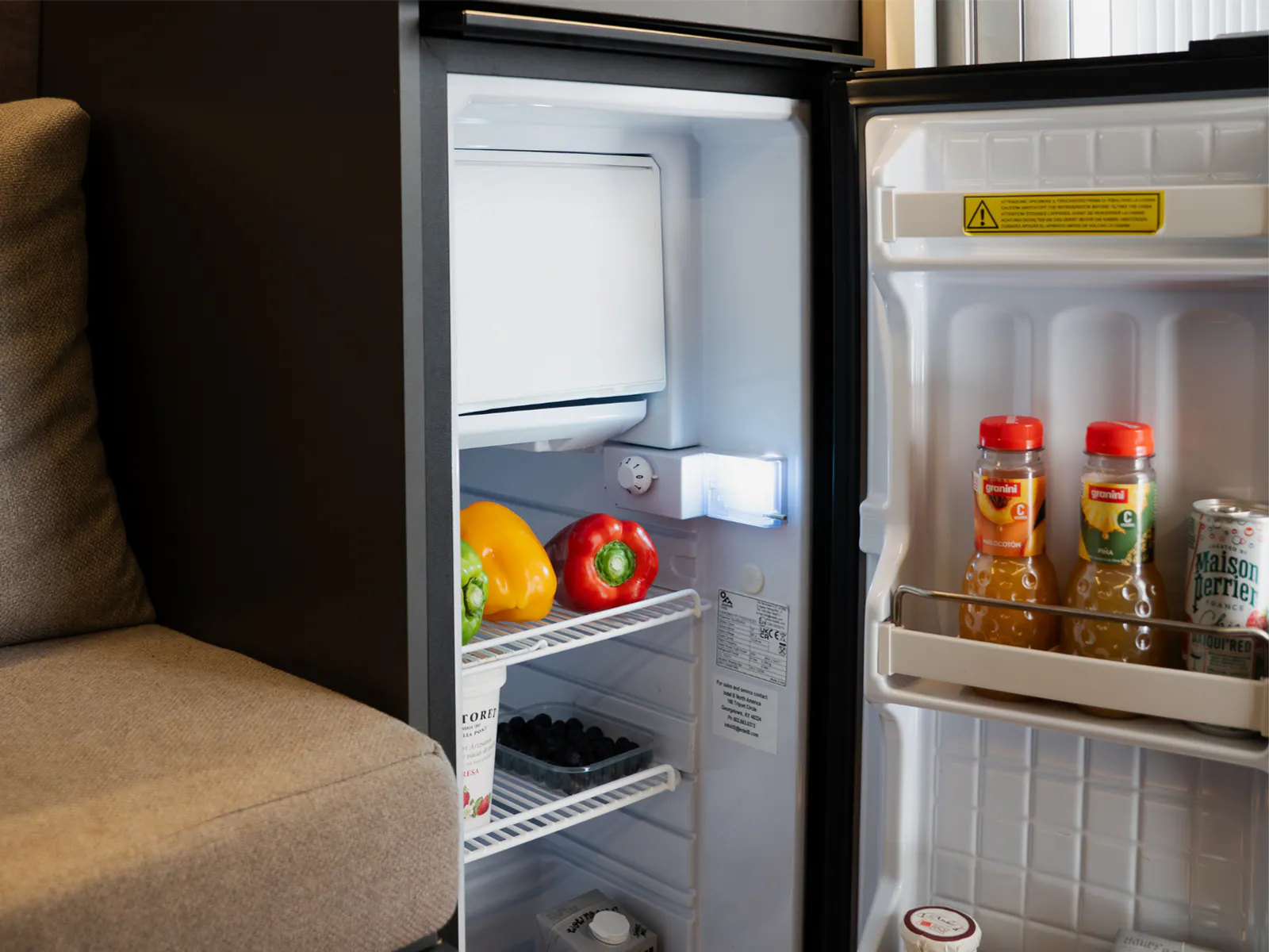 La nevera oberta al costat del sofà, amb aliments i begudes a dins
